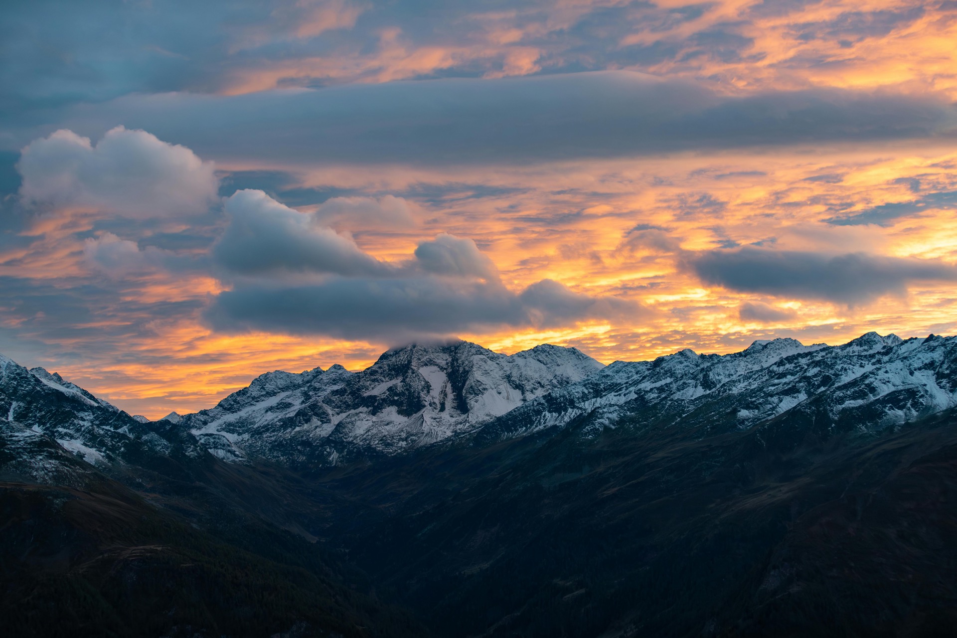 Snow-capped mountains at sunset with dramatic golden clouds